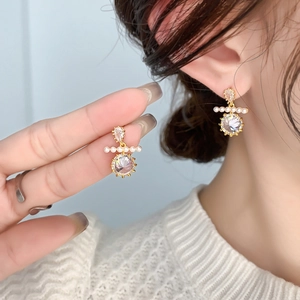 Elegant gold earrings with round moissanite and pearls worn by a model in soft light
