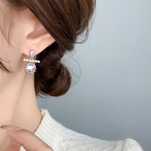 Detail of silver earring featuring five small pearls and a large zircon on a model