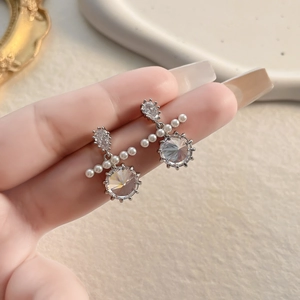 Close-up of elegant moissanite earrings with white pearls and sparkling round cut zircon