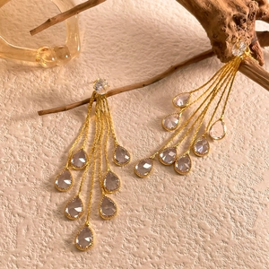 Detail of long gold tassel earrings with teardrop zircons hanging on a wooden branch