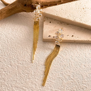 Close-up of long gold tassel earrings with sparkling crystals on textured stone base
