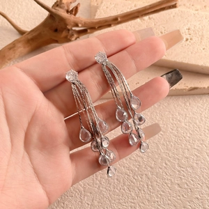 Close-up of silver long tassel earrings with sparkling teardrop crystals on a stone background