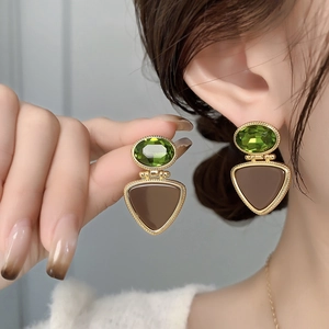 Macro detail of French vintage earrings featuring green gemstones and coffee enamel