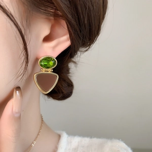 Close-up of vintage gold earrings with oval green gemstone and brown resin pendant
