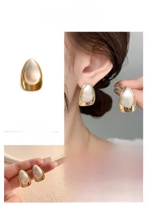 Close-up of gold and silver waterdrop earrings with brushed texture and pearl finish