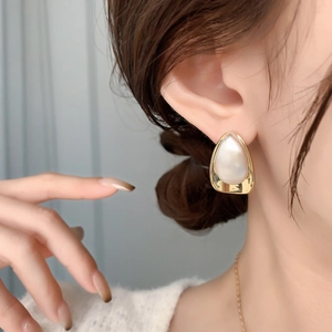 Elegant gold-trimmed teardrop pearl earrings worn by a model in warm lighting