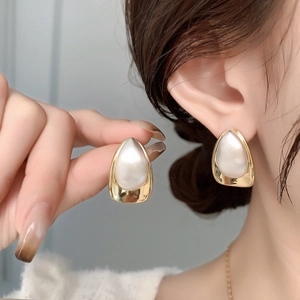 Detailed view of teardrop pearl earrings with gold-toned metal base on model