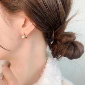 Detail of a 18K gold huggie earring with an irregular surface and an inset white pearl