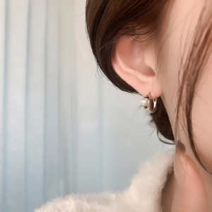 Detailed view of silver hoop earring with pearl accent on model ear in soft lighting
