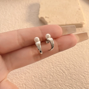 Detail of silver C-shaped earrings with pearls and irregular textured finish on hand