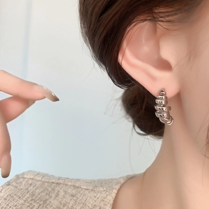 Irregular silver spiral wire C-shaped stud earrings shown as a side-view ear closeup
