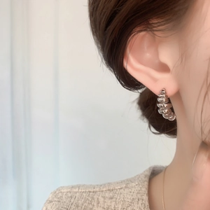 Macro detail of silver irregular wire-wrapped C-shape stud earring on female ear