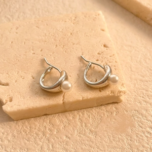 Close-up of irregular textured gold earrings with white pearls on a natural stone base