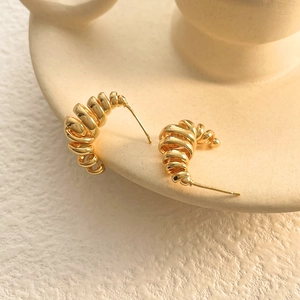 Macro view of gold spiral earring with a polished 3D twist design on ceramic tray