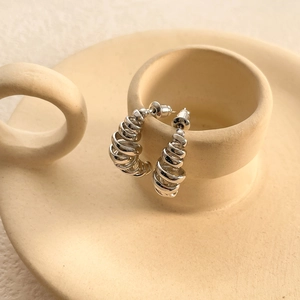 Close-up of silver irregular spiral C-shaped hoop earrings on a ceramic cup edge