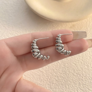 Macro shot showing the irregular silver wire-wrap C-shaped stud earrings held by hand