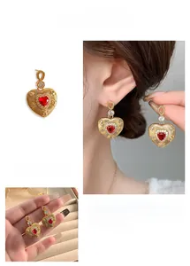 Close-up of heart-shaped gold earrings featuring a red gem and zircon accents