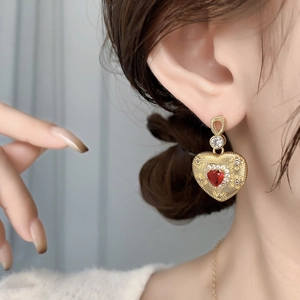 Detailed view of heart-shaped gold earring with red gemstone and radiant metal texture