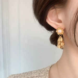 Close-up of golden pearl tassel earrings featuring metallic leaves worn on a model