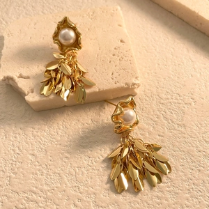 Macro shot of gold leaf tassel earrings with white pearls on a textured stone surface