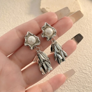 Detailed view of silver leaf tassel earrings with white pearl studs on a stone display