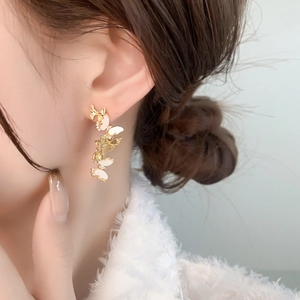 Dettaglio degli orecchini pendenti a farfalla in oro con accenti in smalto bianco
