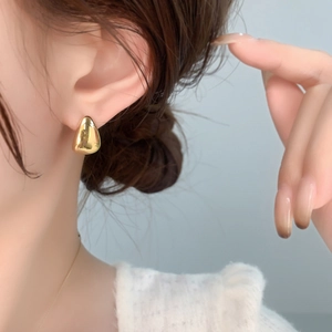 Close-up of minimalist gold teardrop earrings with a polished mirror finish on a model
