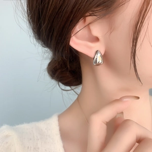 Close-up of minimalist silver water drop earring worn by model on blue background