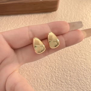 Minimalist teardrop earrings in polished gold finish held between fingers on a warm beige background