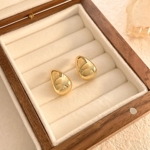 Macro shot of gold teardrop earrings with mirror finish in a wooden jewelry box