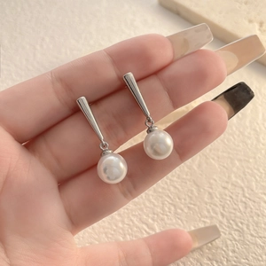 Macro detail of elegant drop earrings featuring polished silver metal rods and white pearls