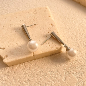 Close-up of pearl drop earrings with cone pendants on a natural stone display board
