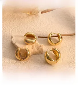 Close-up of golden chunky hoop earrings with wavy texture on natural stone and branch