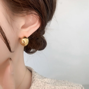 Close-up of minimalist gold spherical stud earring showing glossy metallic finish and texture