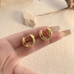 Polished gold thick hoop earrings held against a minimalist beige stone background