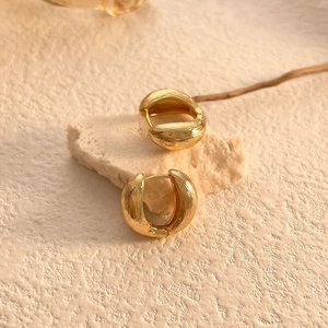Close-up of gold hoop earrings with lava texture on white stone pedestal display