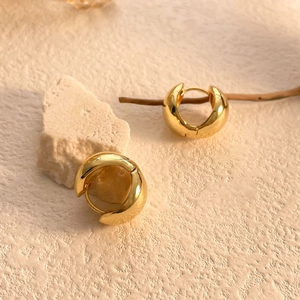 Macro detail of chunky gold hoop earrings on natural white stone and wood decor