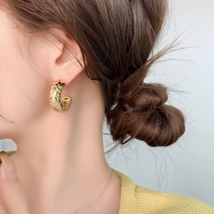 Detail of gold C-shaped earrings with woven texture and micro-inlaid cubic zirconia