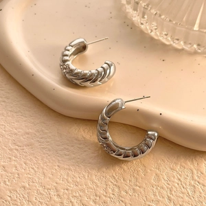 Detail of silver twisted rope hoop earrings on a decorative wavy ceramic tray