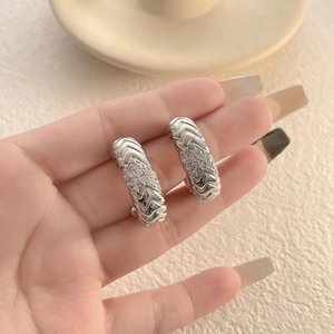Macro detail of silver snake bone hoop earrings with micro-set zircons on warm background