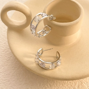 Detail view of silver C-shaped earrings with micro-set stones on ceramic stand