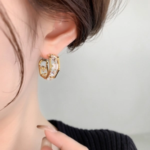 Close-up of gold geometric earrings with square white gemstones and micro-pave detailing
