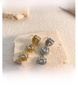 Close-up of triple heart drop earrings with zircons in gold and silver finishes