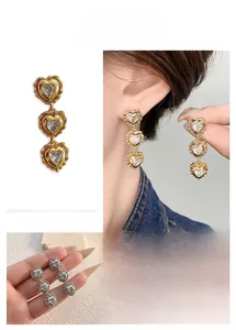 Detailed view of triple heart drop earrings with inset cubic zirconia stones