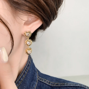 Close-up of triple heart drop earrings in gold finish with sparkling zircons on model