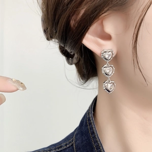 Elegant silver triple heart drop earrings with sparkling rhinestones worn by a model