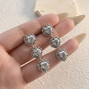 Close-up of long silver heart earrings featuring three tiered sparkling zircon heart gems