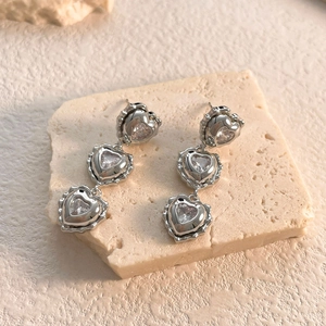 Macro shot of silver heart drop earrings with sparkling crystals on beige stone texture