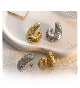 Macro di orecchini a perno astratti oro e argento con texture su vassoio in ceramica