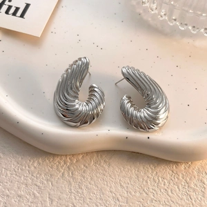 Dettaglio di orecchini a C in argento con texture a spirale su un vassoio di ceramica